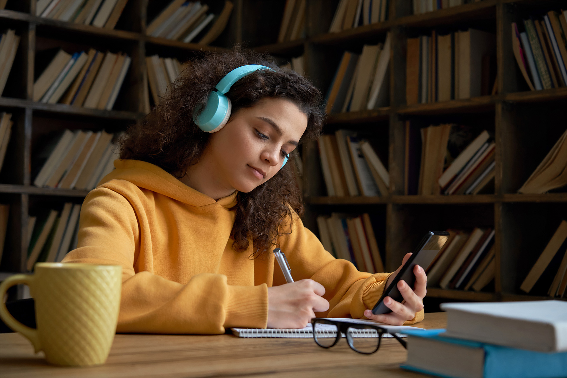 Student hard at work studying, referencing QuizPrep on her phone in one hand and taking notes with the other.