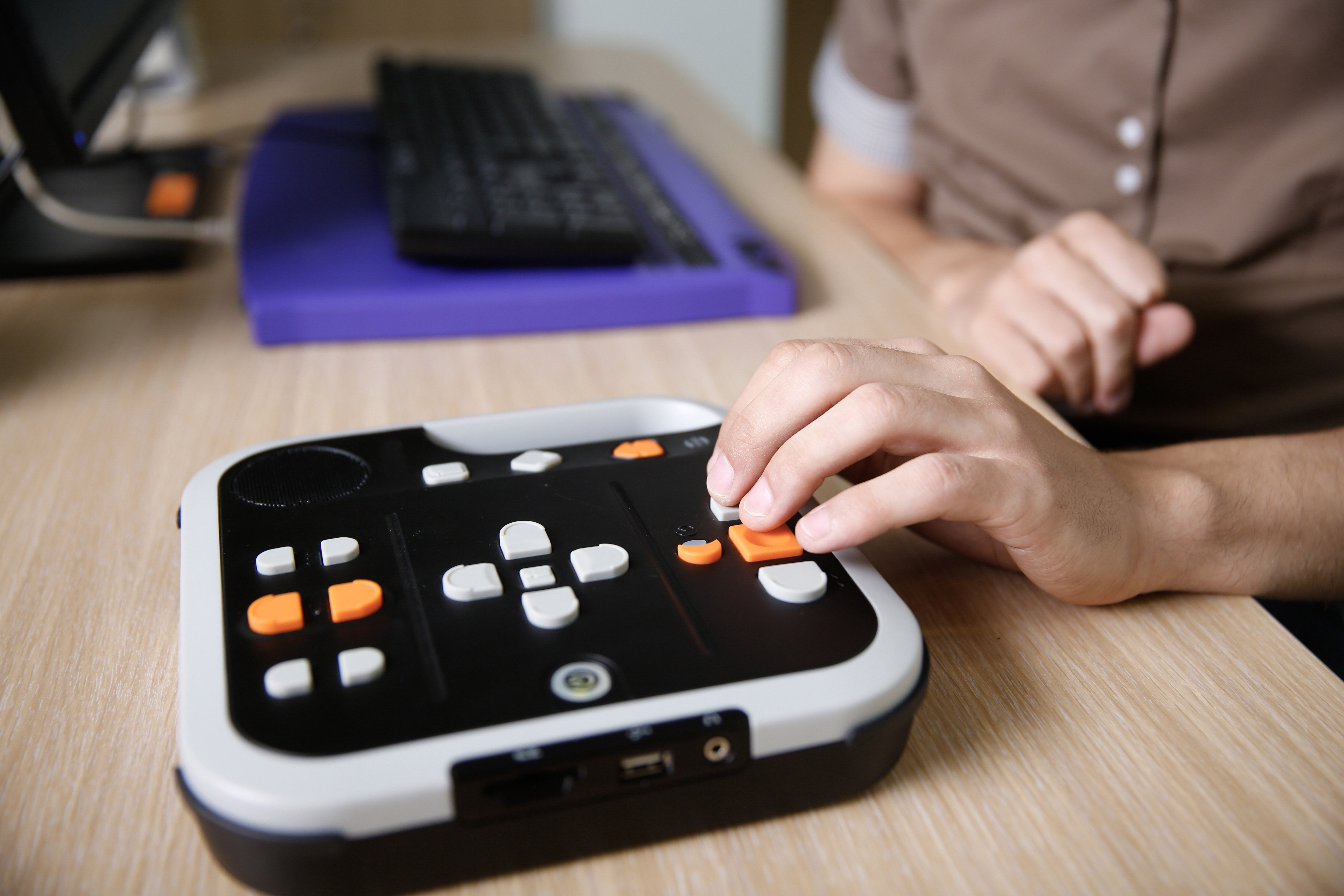 hand pressing large arrow buttons on keypad accessibility tool for audio books, includes text-to-speech capabilities